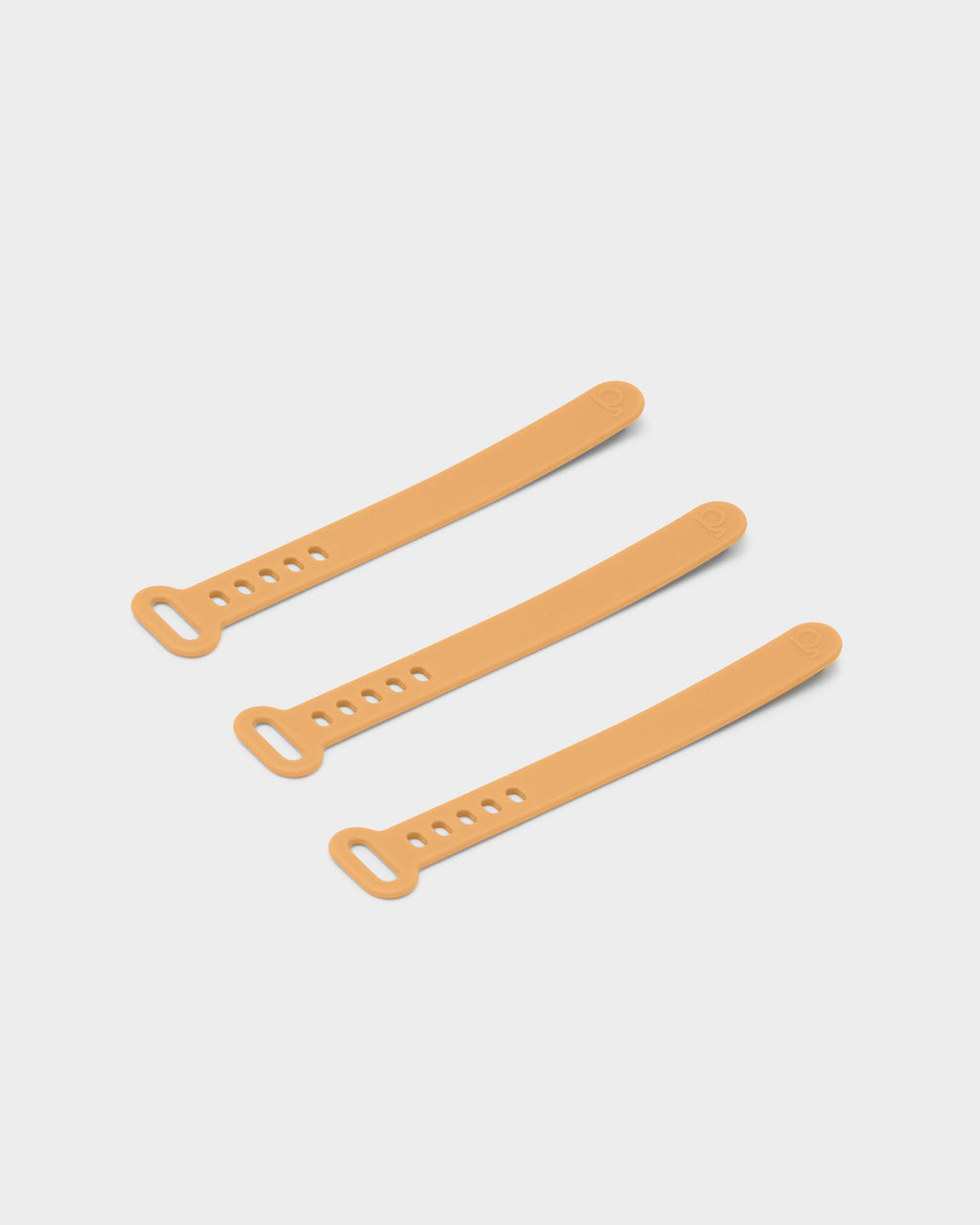 Three apricot silicone cable ties arranged diagonally on a light grey studio background, showing loop ends and peg holes
