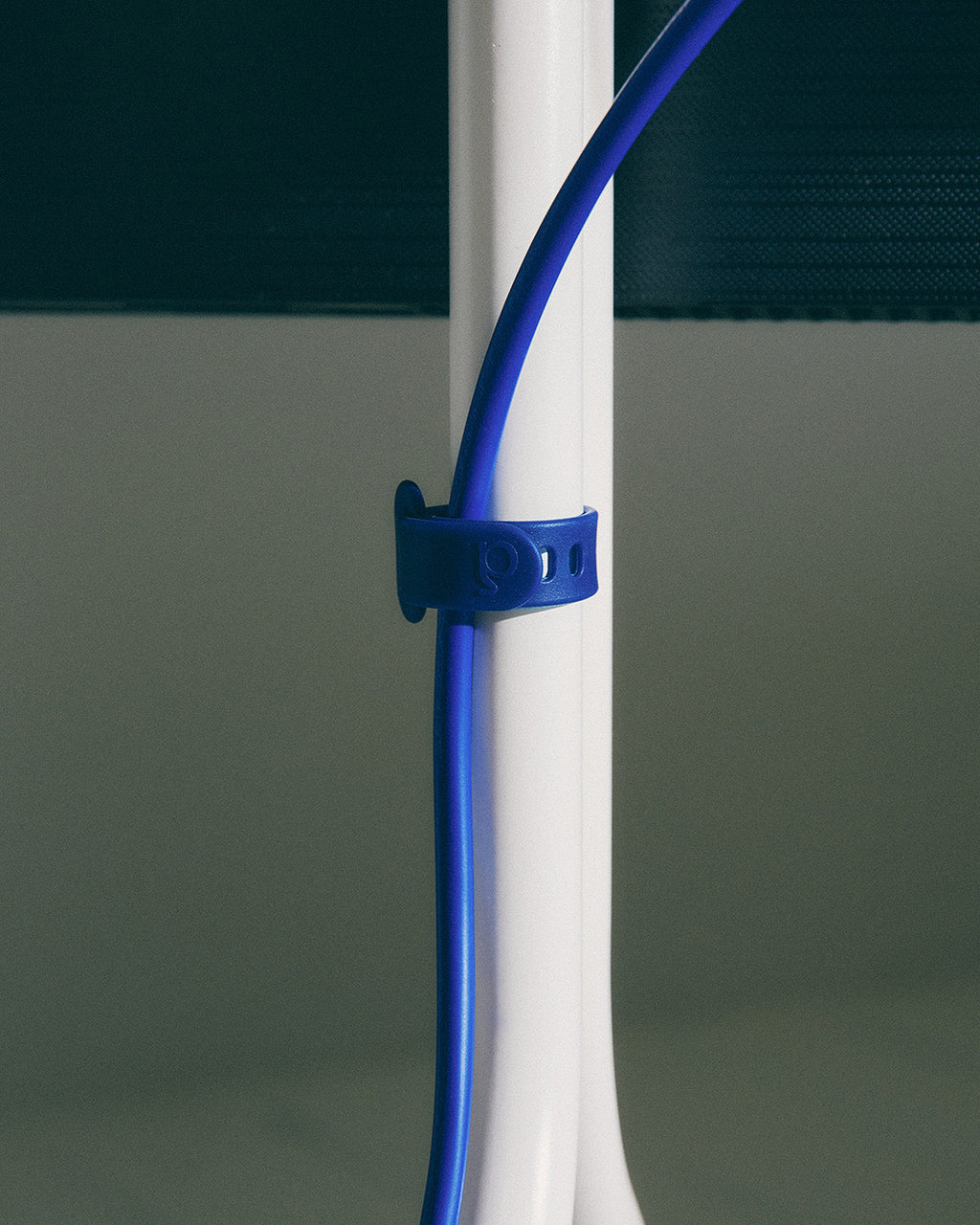 Blue Cable Tie fastened around a white table leg, securing a blue cable in a close-up lifestyle detail shot
