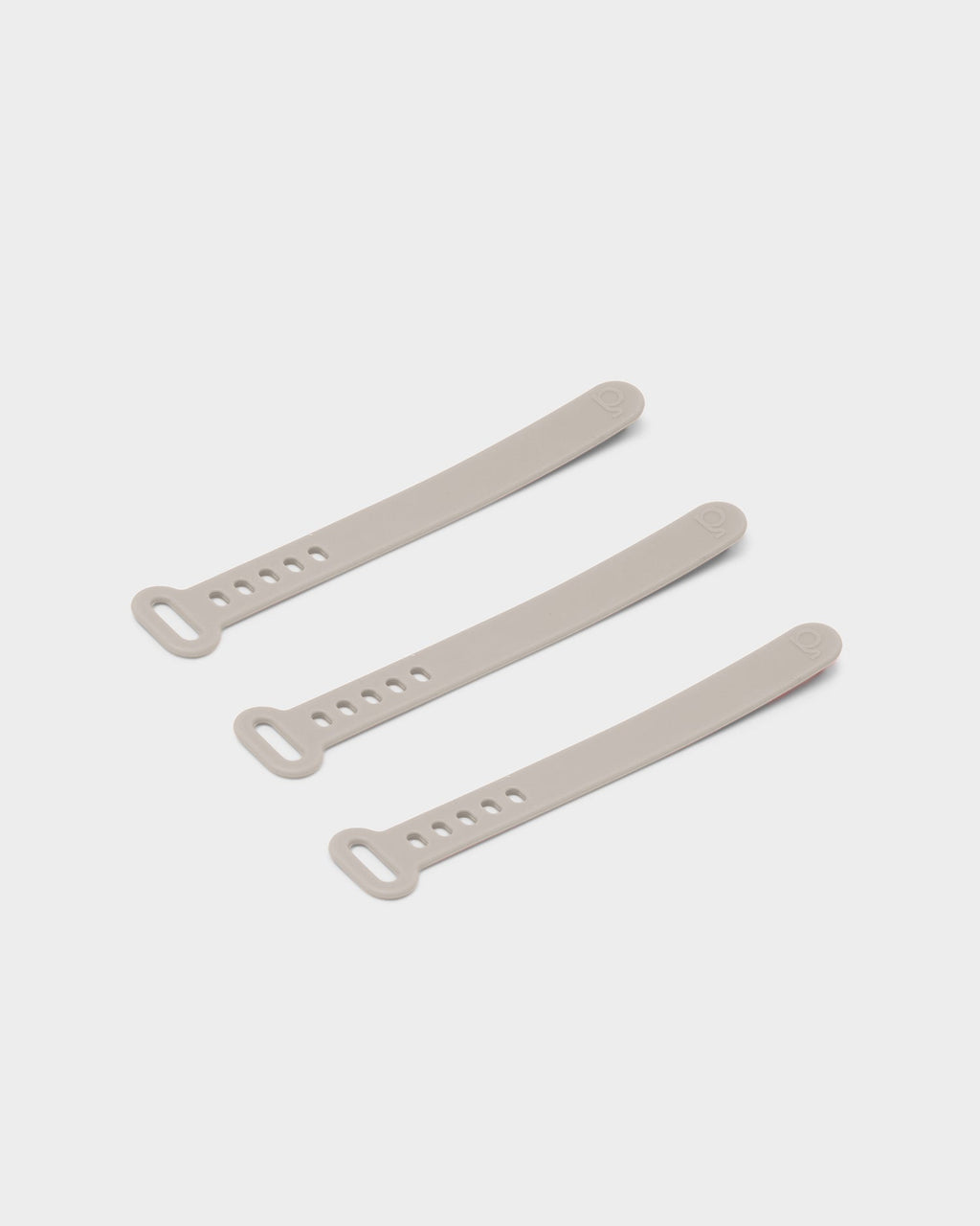 Three Cable Tie straps in Oat arranged diagonally on a light studio backdrop, showing looped ends and adjustment holes