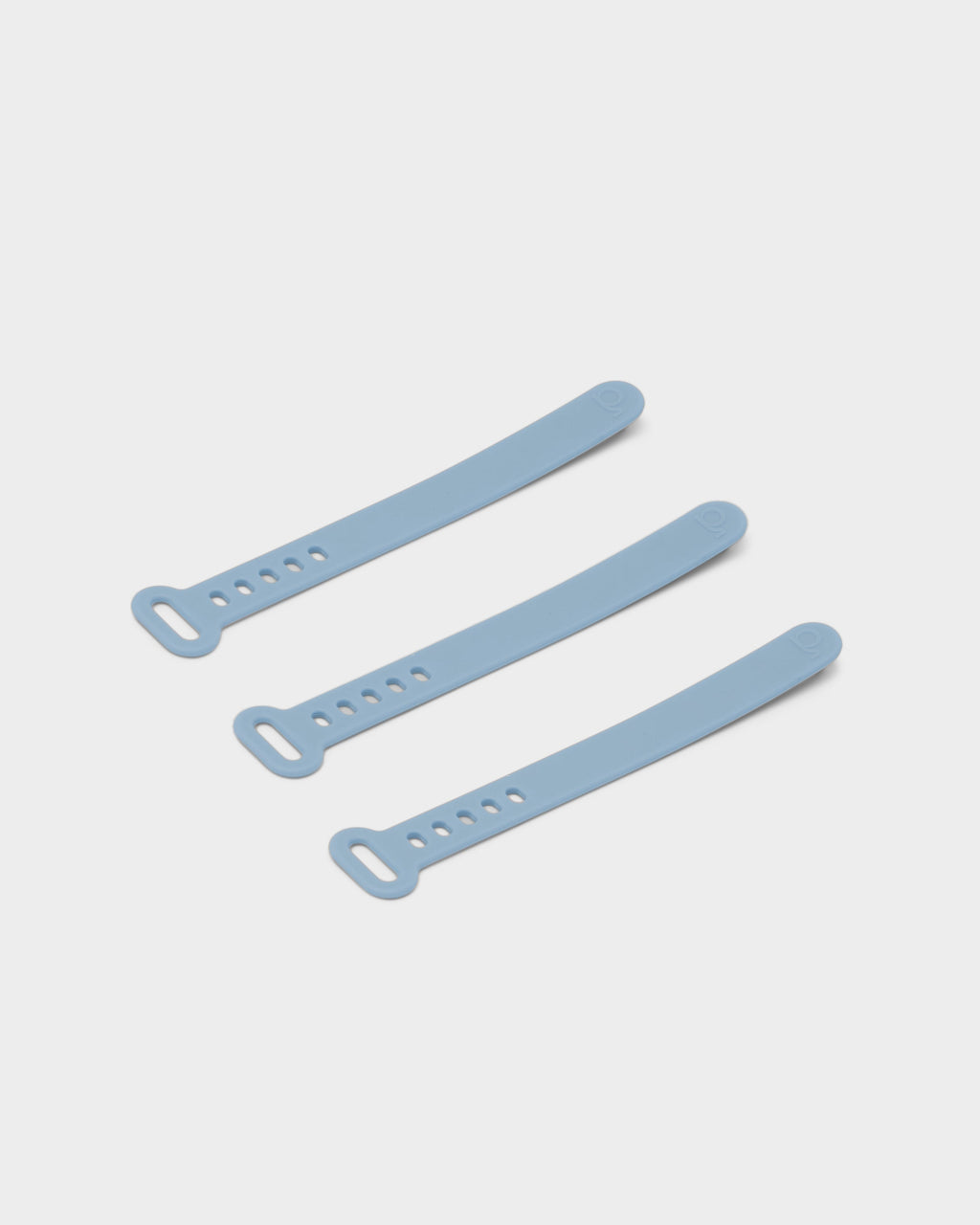 Three Powder Blue silicone cable ties arranged diagonally on a light grey studio background, showing peg holes and loop ends