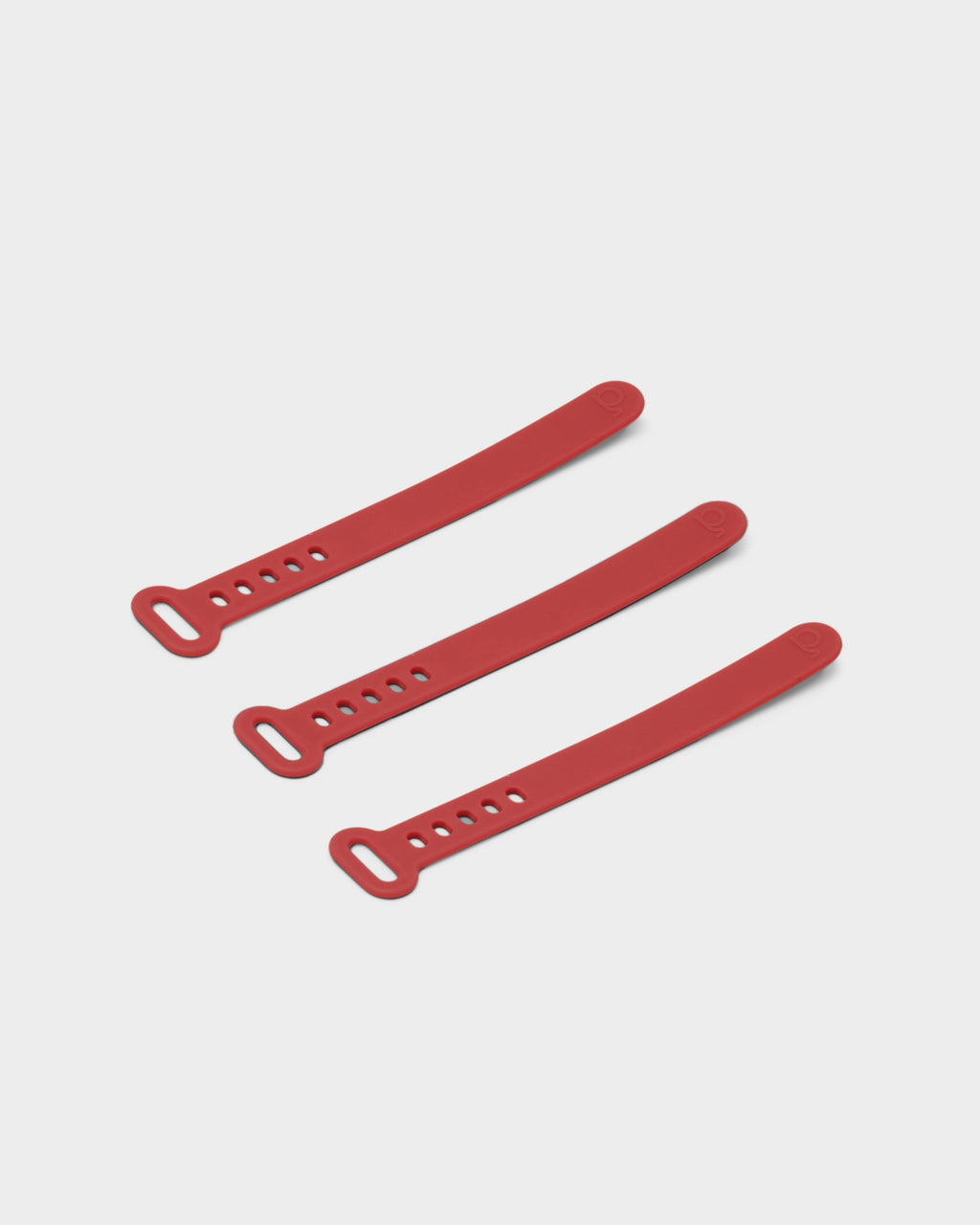 Three Burnin' Red silicone Cable Ties laid diagonally on a light grey studio background, showing loop ends and holes