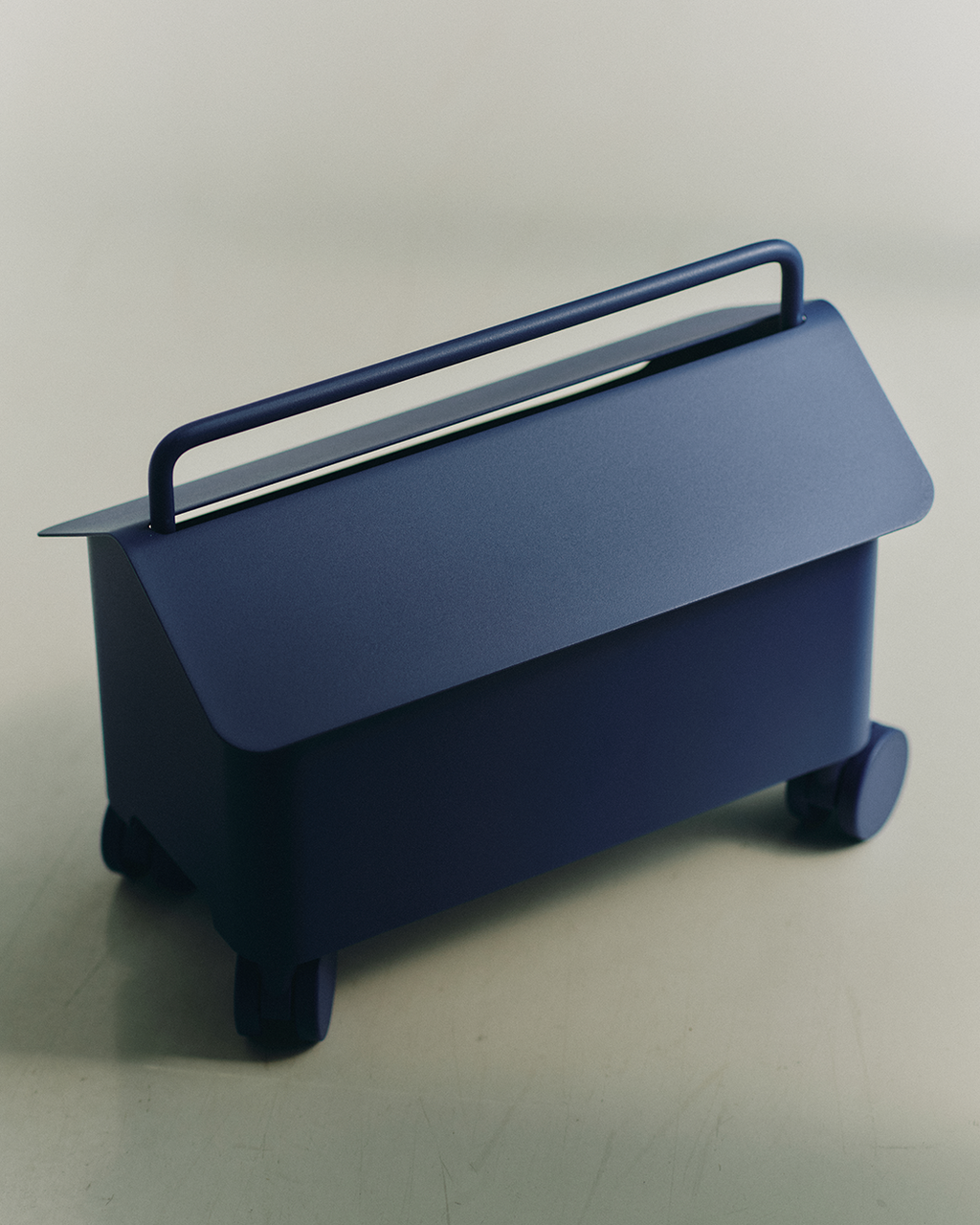 Cable Villa in Ultra Marine shown at an angle in a studio setting, with lifted lid, carry handle and rolling casters