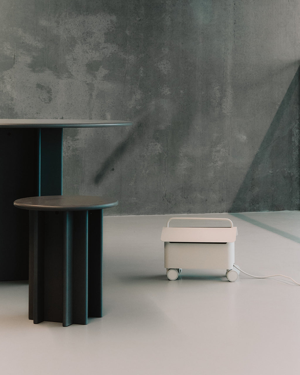Cable Villa in Pearl on castors beside dark round side tables in a concrete-walled room, cord trailing out
