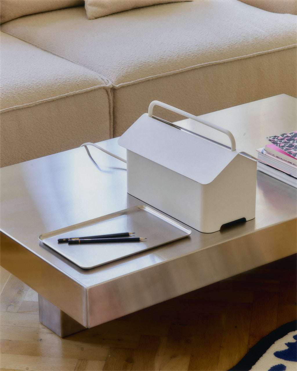 Cable Villa in Pearl on a steel coffee table beside a tray of pencils and books, beige sofa behind in a bright living room
