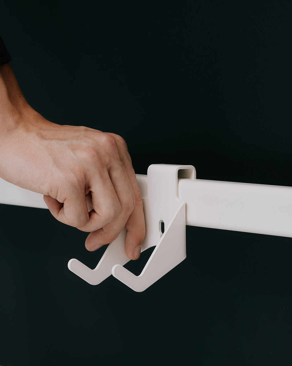 Hand slotting the white Controller Mount onto a wall rail against a charcoal backdrop, dual hooks in focus