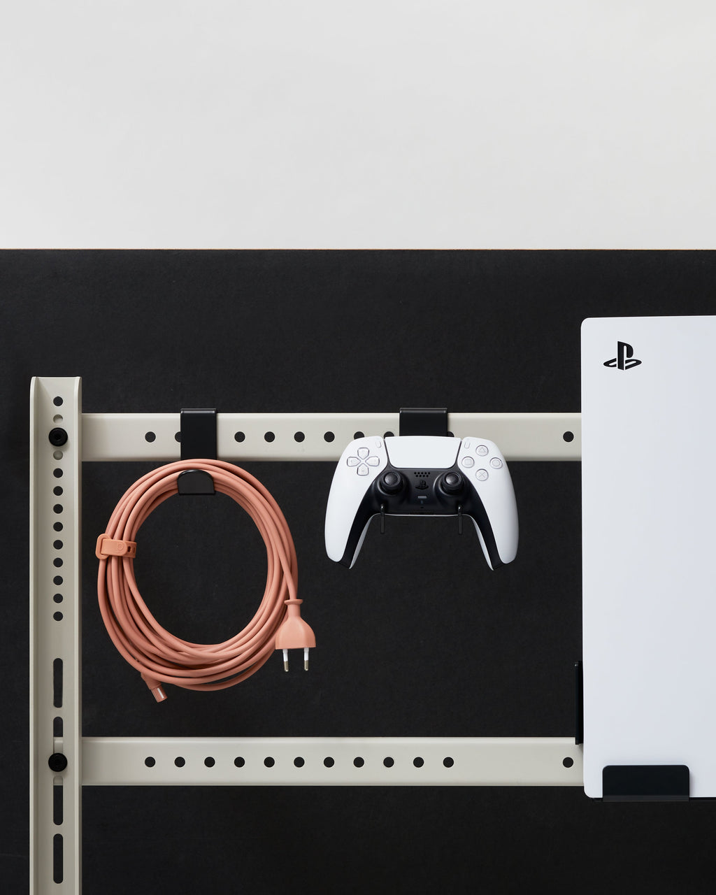 Charcoal Controller Mount holding a white gamepad on a wall rail beside a coiled cable and PS5 console