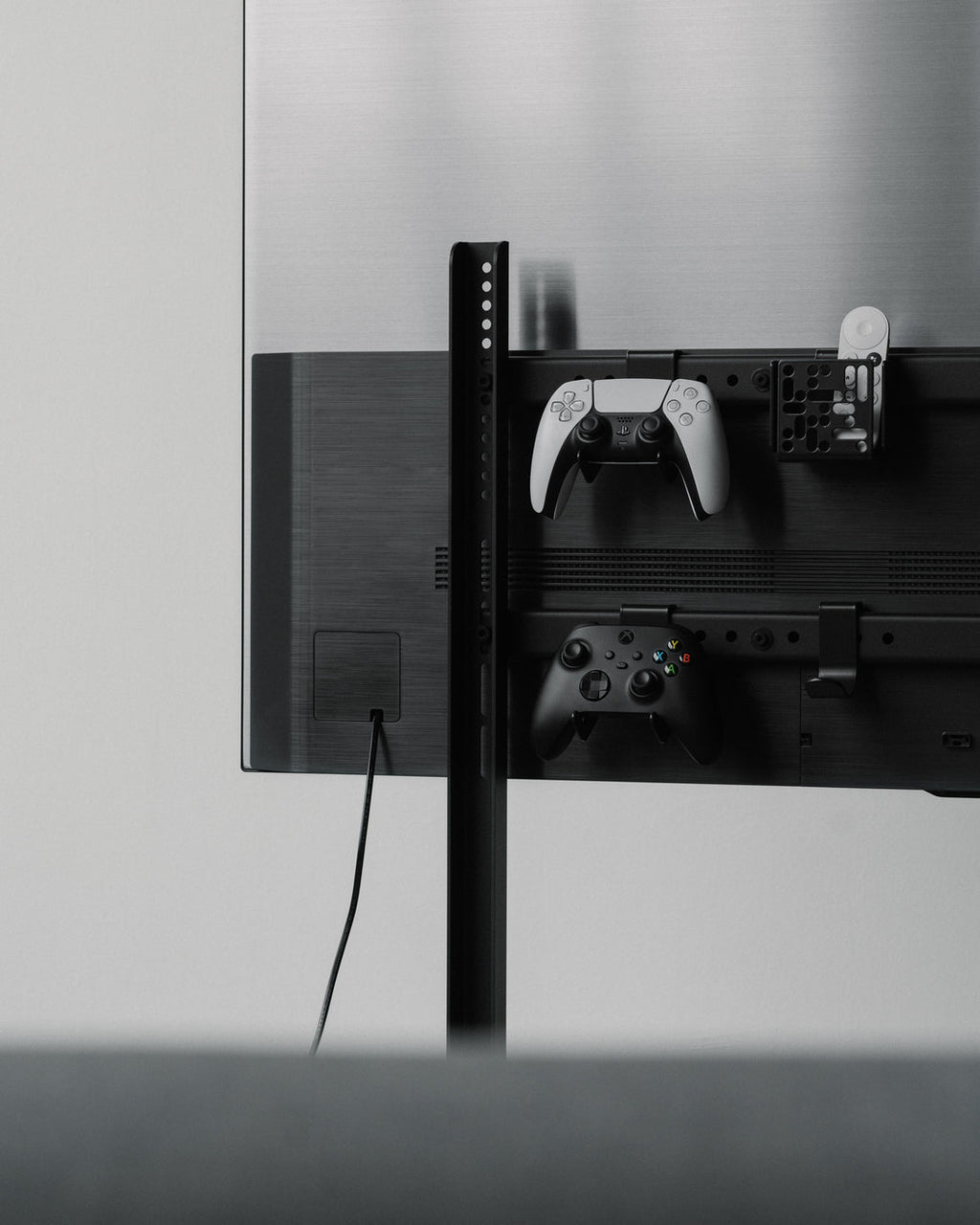 Pearl Controller Mount holding PlayStation and Xbox controllers on the rear rail of a wall-mounted TV setup
