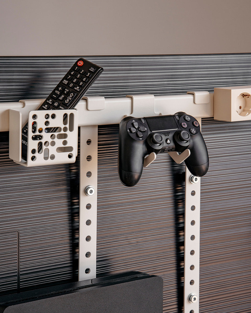 Pearl Controller Mount holding a PS4 controller on a wall rail beside a remote holder in a modern living room setup