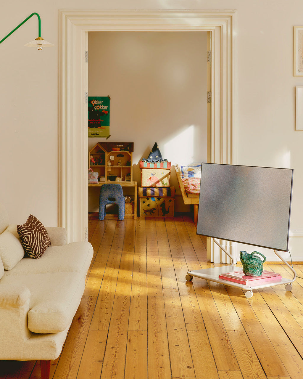 Disco in Oat rolling TV stand with wheels holding a mounted flatscreen in a sunlit living room beside a cream sofa