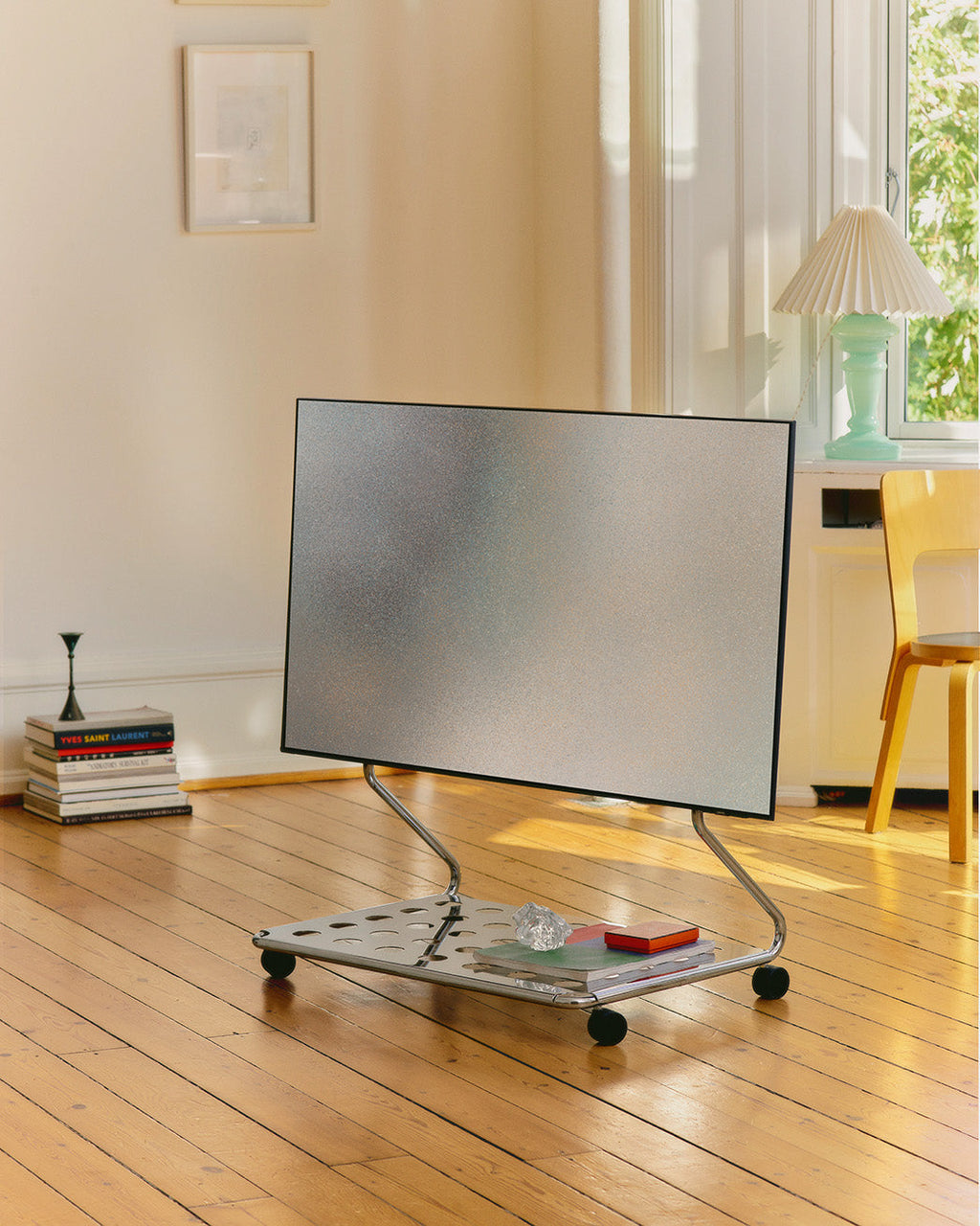 Disco chrome TV stand on wheels holding a flatscreen in a sunlit wood-floor living room, angled side view