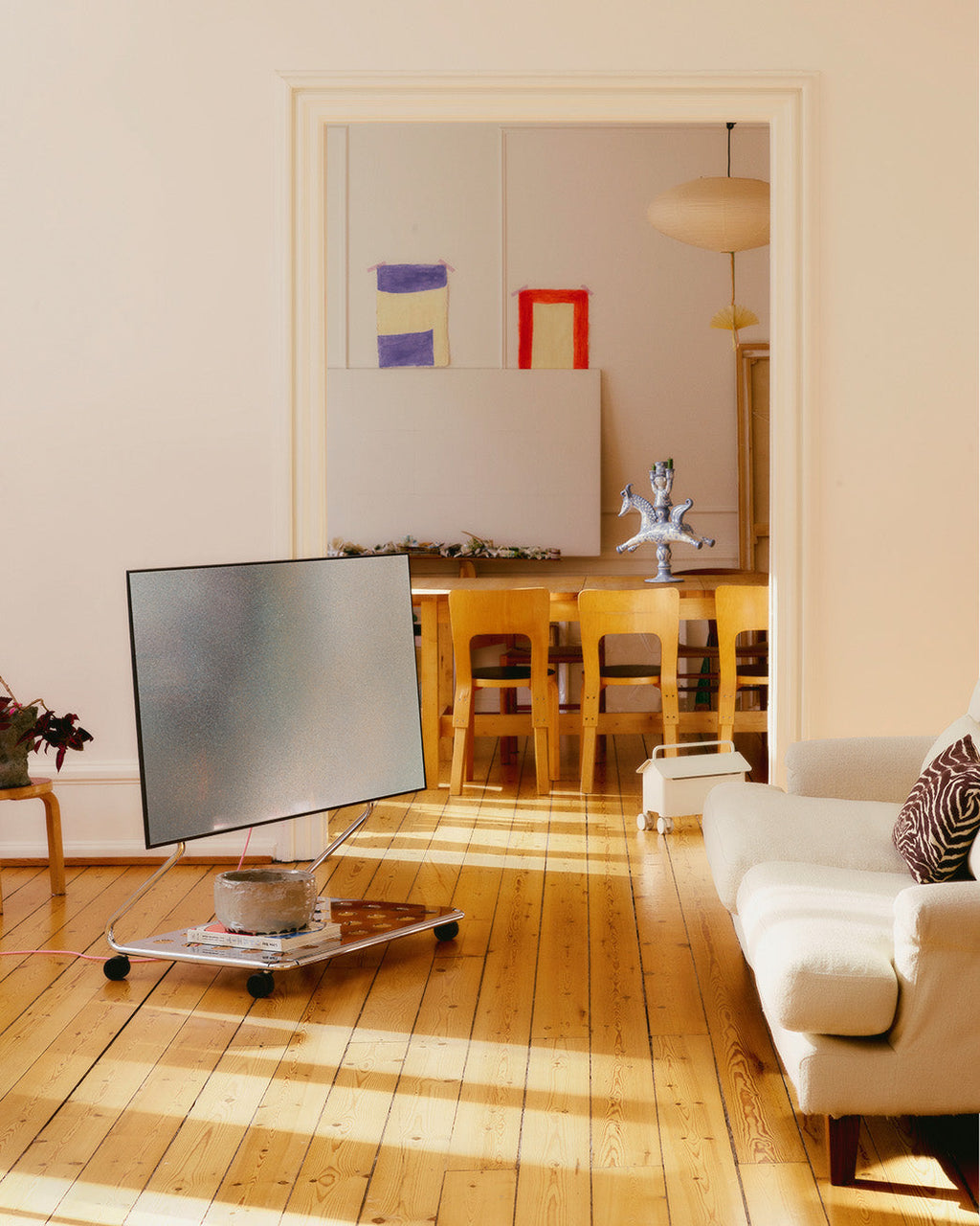 Disco chrome rolling TV stand holding a flat screen in a sunlit living room with wood floors and cream sofa
