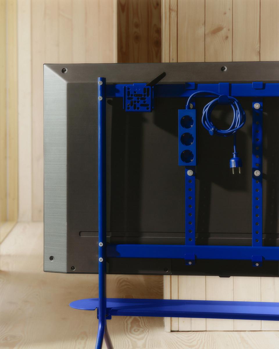 Rear view of a TV on the Ultra Marine Hook Mount, showing blue frame, power strip and coiled cable in a wood-panelled room