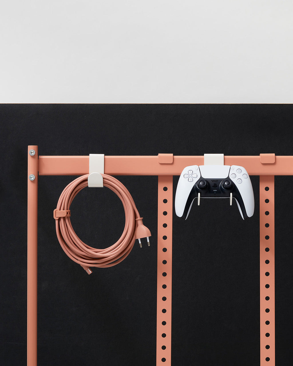 Pearl Hook Mounts on a coral wall rail holding a coiled cable and a white game controller against black panel