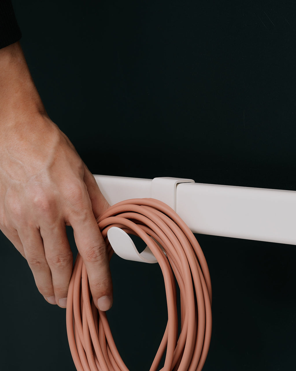 Hand hanging a coiled terracotta hose on an Oat Hook Mount attached to a white rail, dark studio backdrop