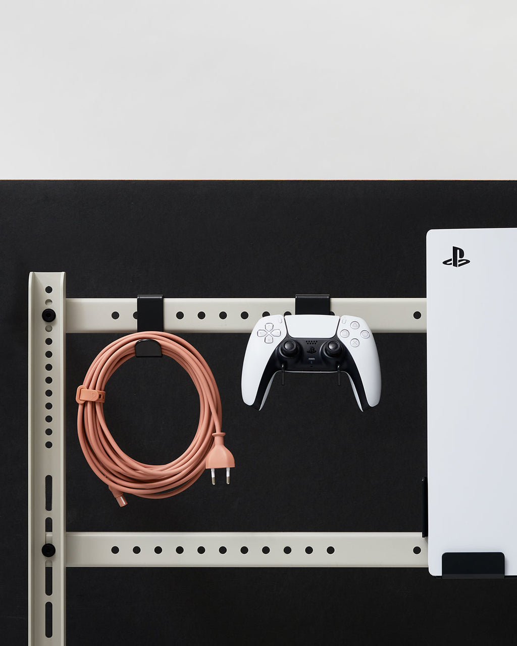 Hook Mount in Powder Blue on a wall rail system holding a coiled cable and PS5 controller beside a mounted console