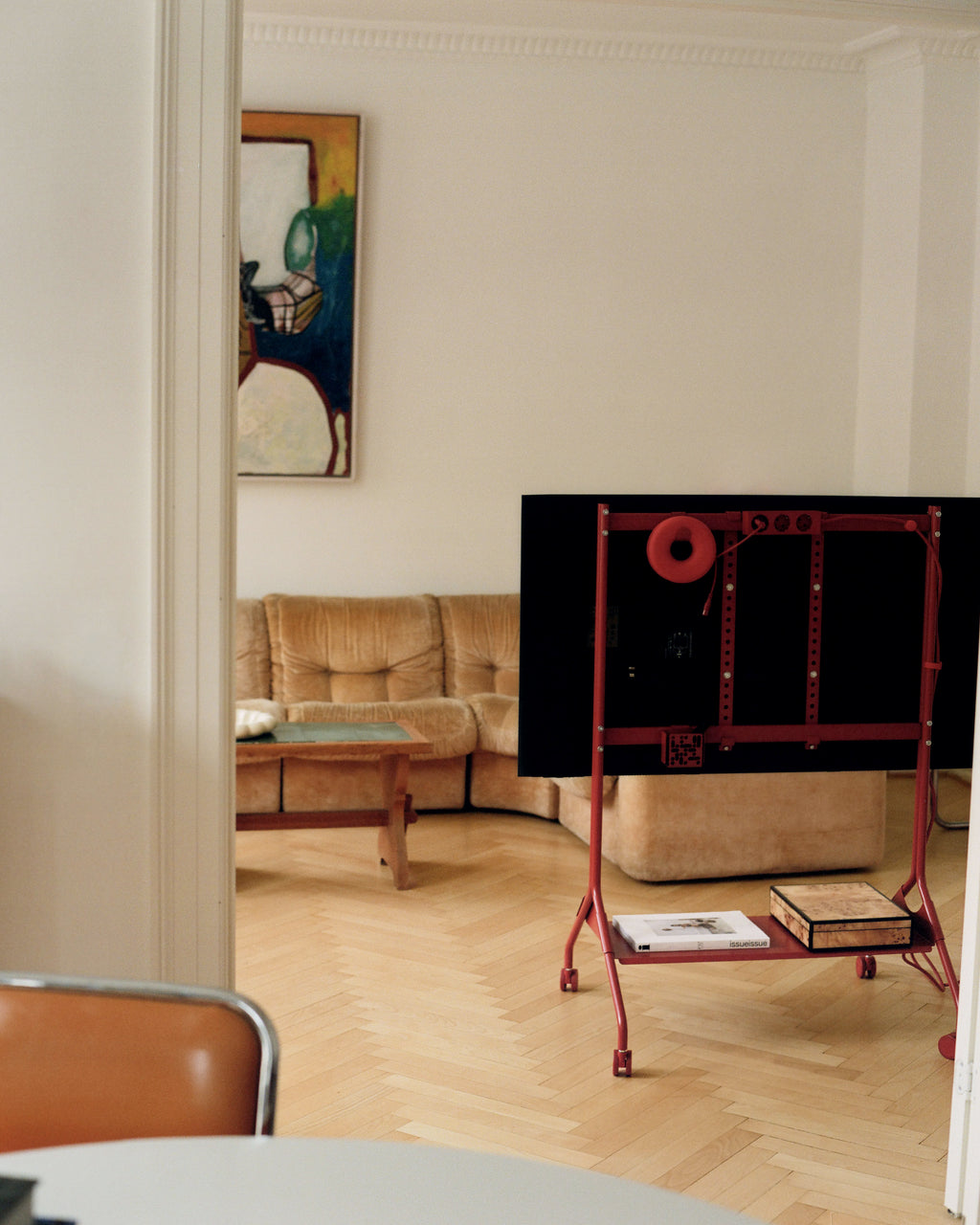 Rear view of Hook Mount in Burnin' Red on wheels holding a TV in a living room, with books on its lower shelf