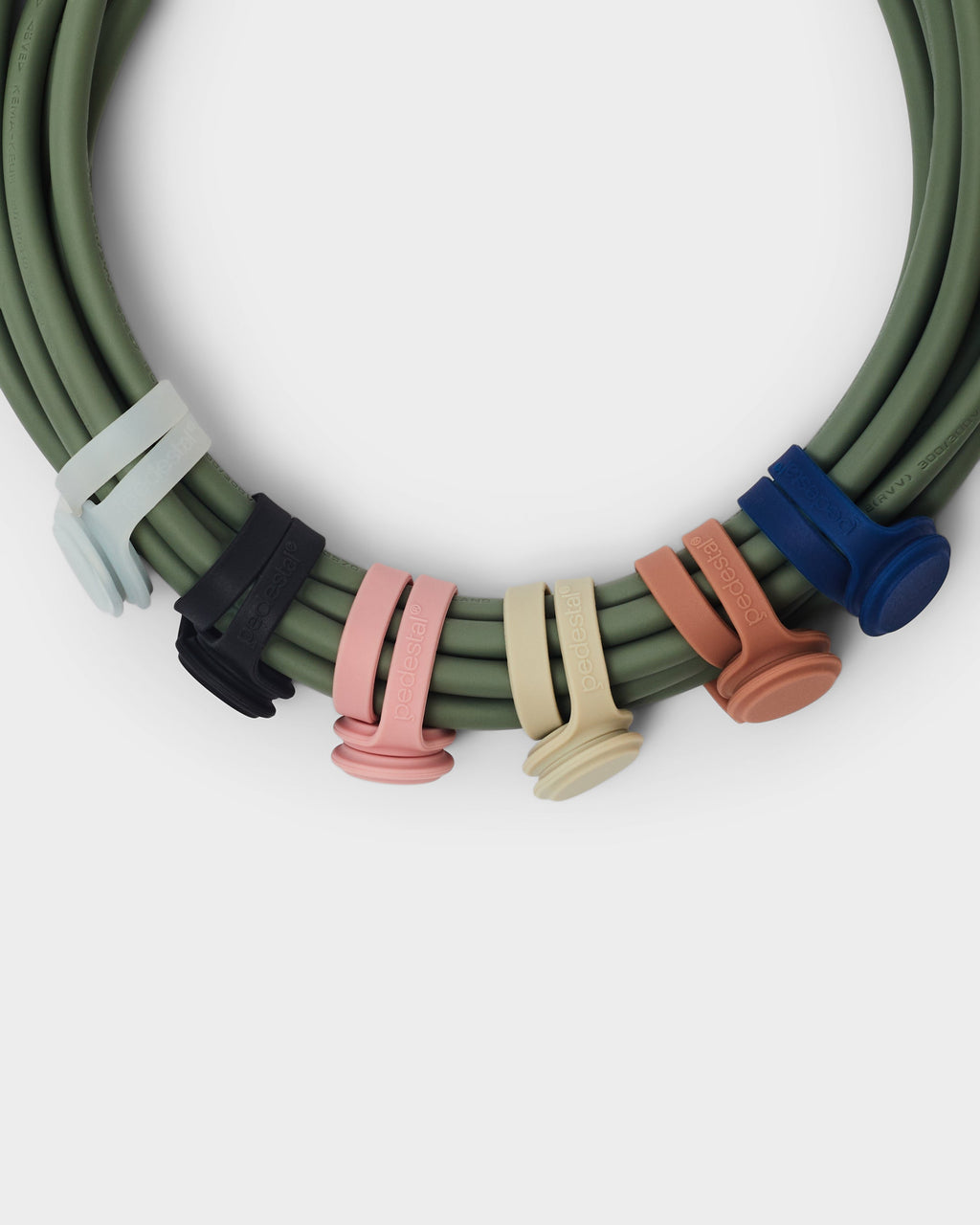 Six Magnetic Cable Ties in assorted colors gripping a coiled mossy green cable, overhead studio close-up