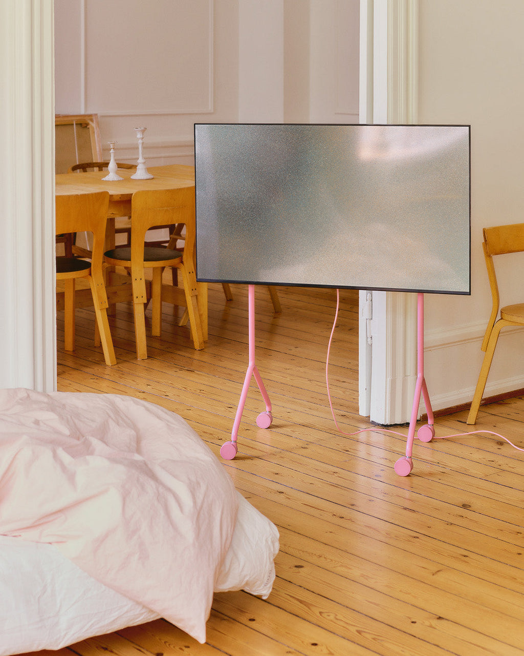 Moon Light TV stand in Bubble Gum pink holding a flatscreen on castor wheels in a sunlit bedroom with wood floors