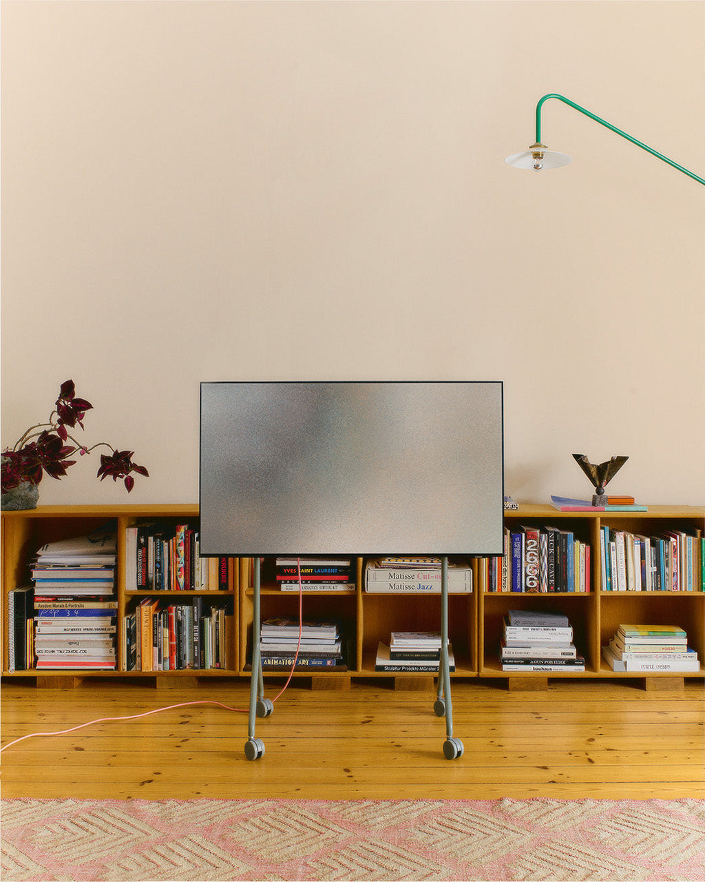 Mossy Green Moon Light TV stand on wheels holding a flatscreen in a living room with low bookshelves and pine floor