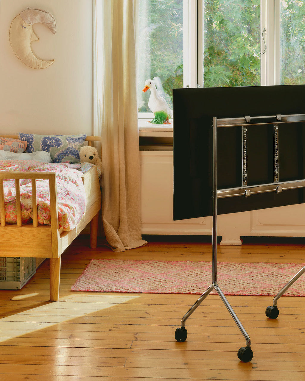 Oat Moon Light hangs on a child's bedroom wall beside a bed, with a black TV on a chrome rolling stand in view