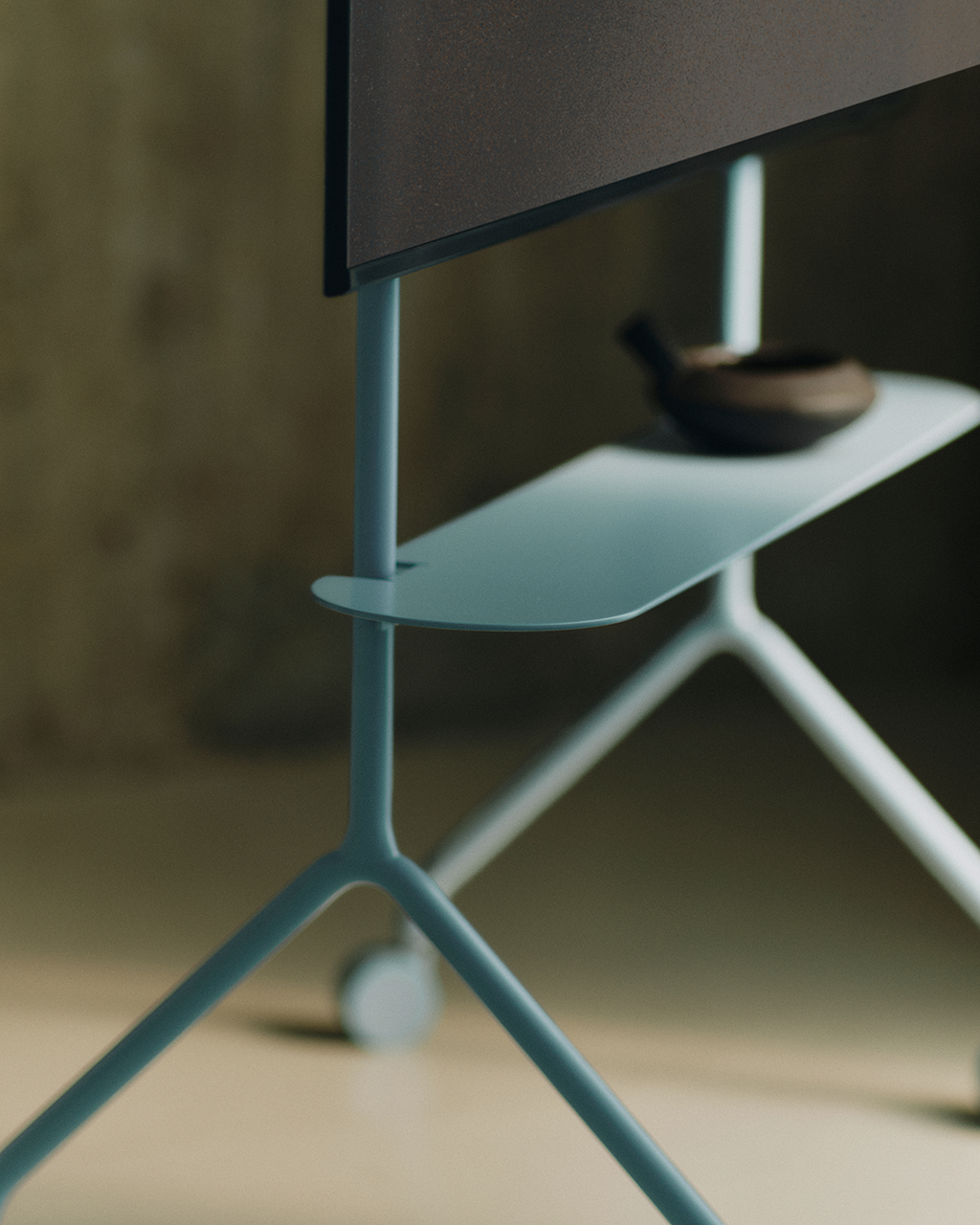 Close-up of the Moon Light TV stand in Powder Blue, showing its shelf with a bowl, splayed legs and caster wheel