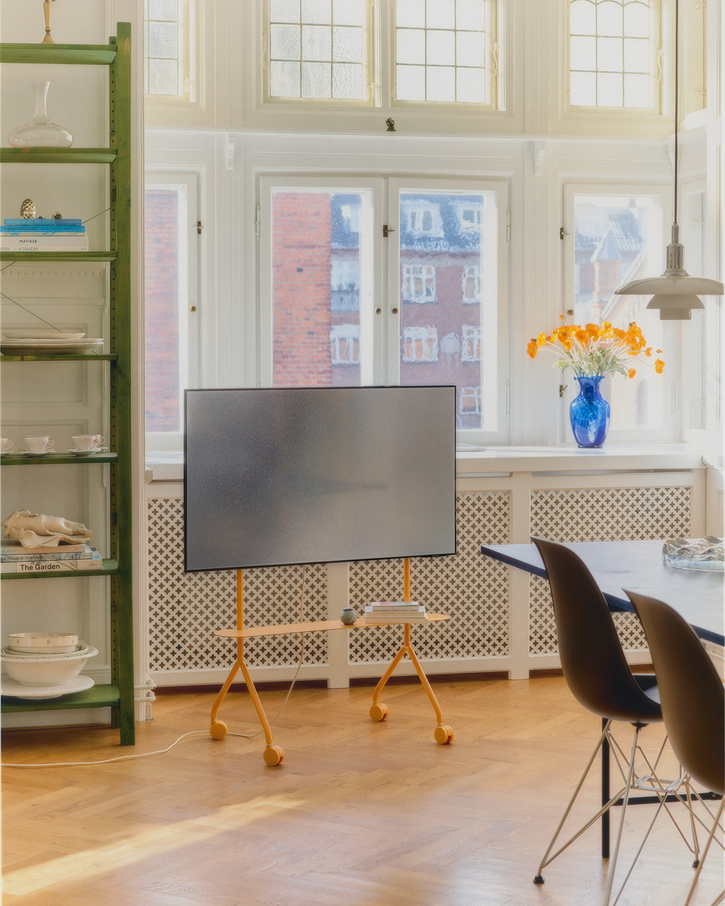 Moon Light Shelf in Apricot holding a mounted TV on wheels in a sunlit dining room with herringbone floors and books