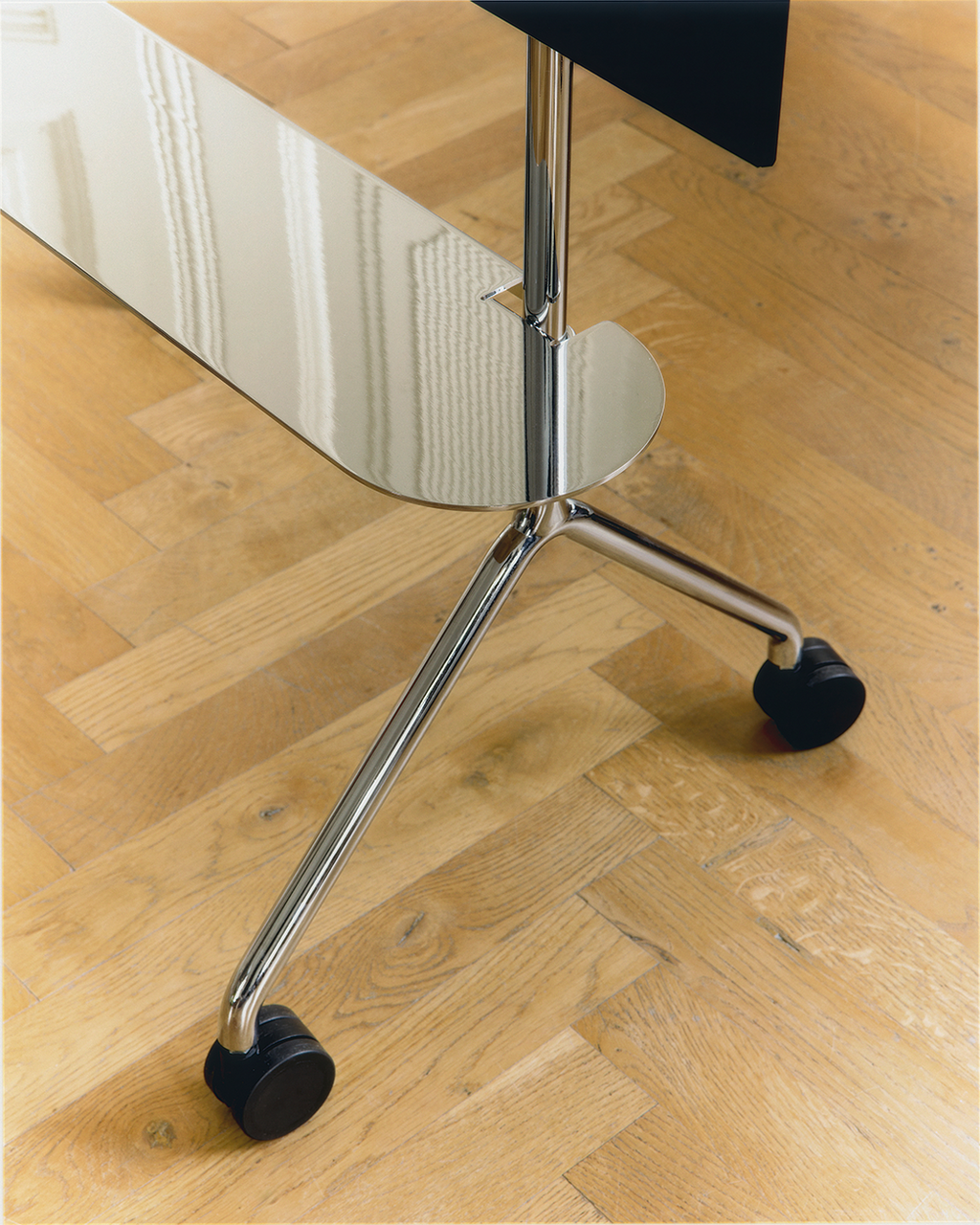 Close-up of the Moon Light Shelf in Oat, showing polished chrome tripod legs and black castor wheels on parquet flooring