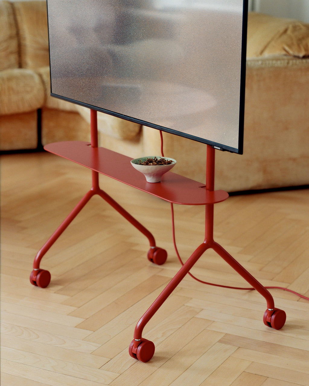 Moon Light Shelf in Burnin' Red holding a TV on castors in a living room, low angle showing legs and wheels