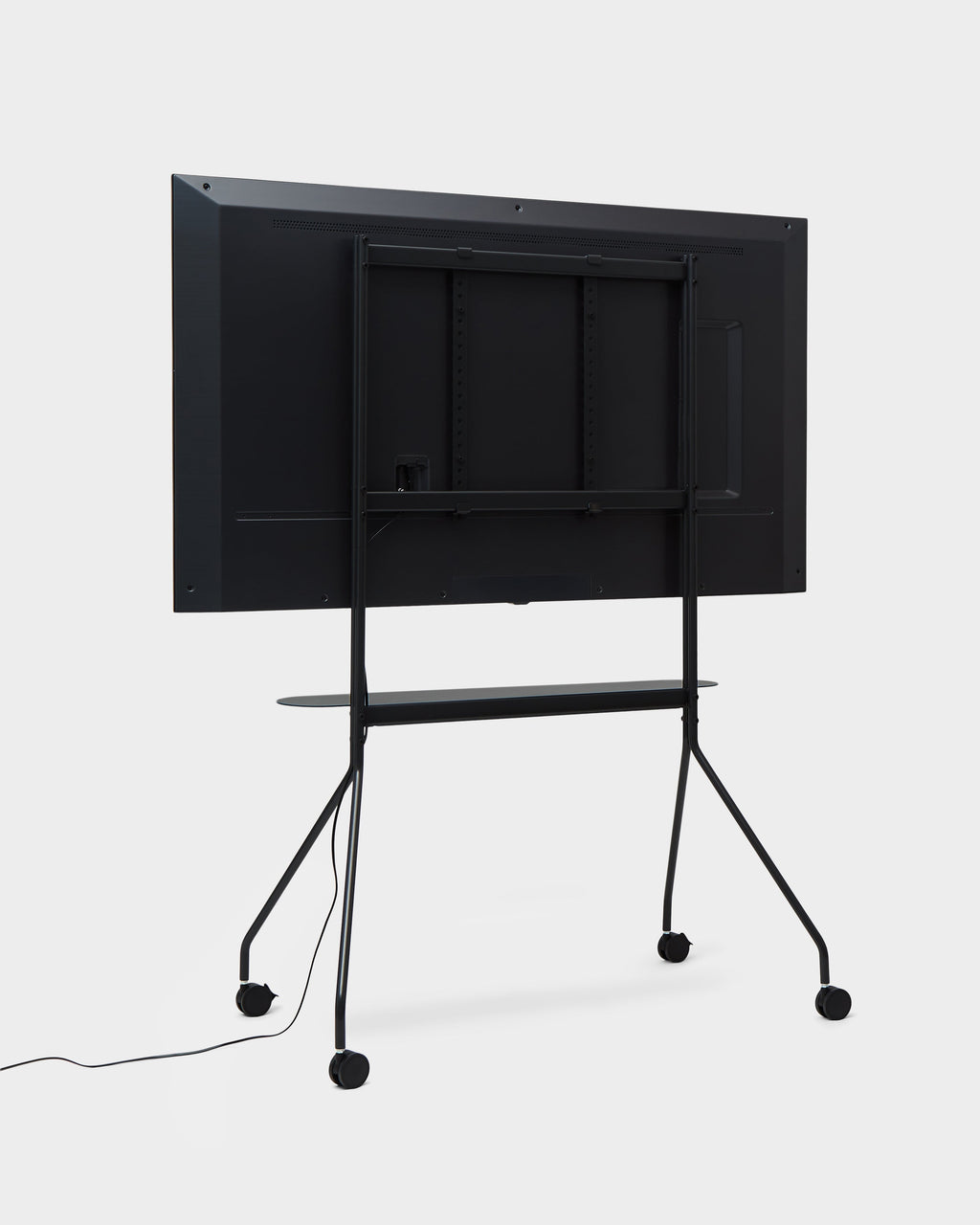 Rear view of Moon PRO stand in Charcoal holding a mounted TV, showing shelf, cable and locking wheels in studio