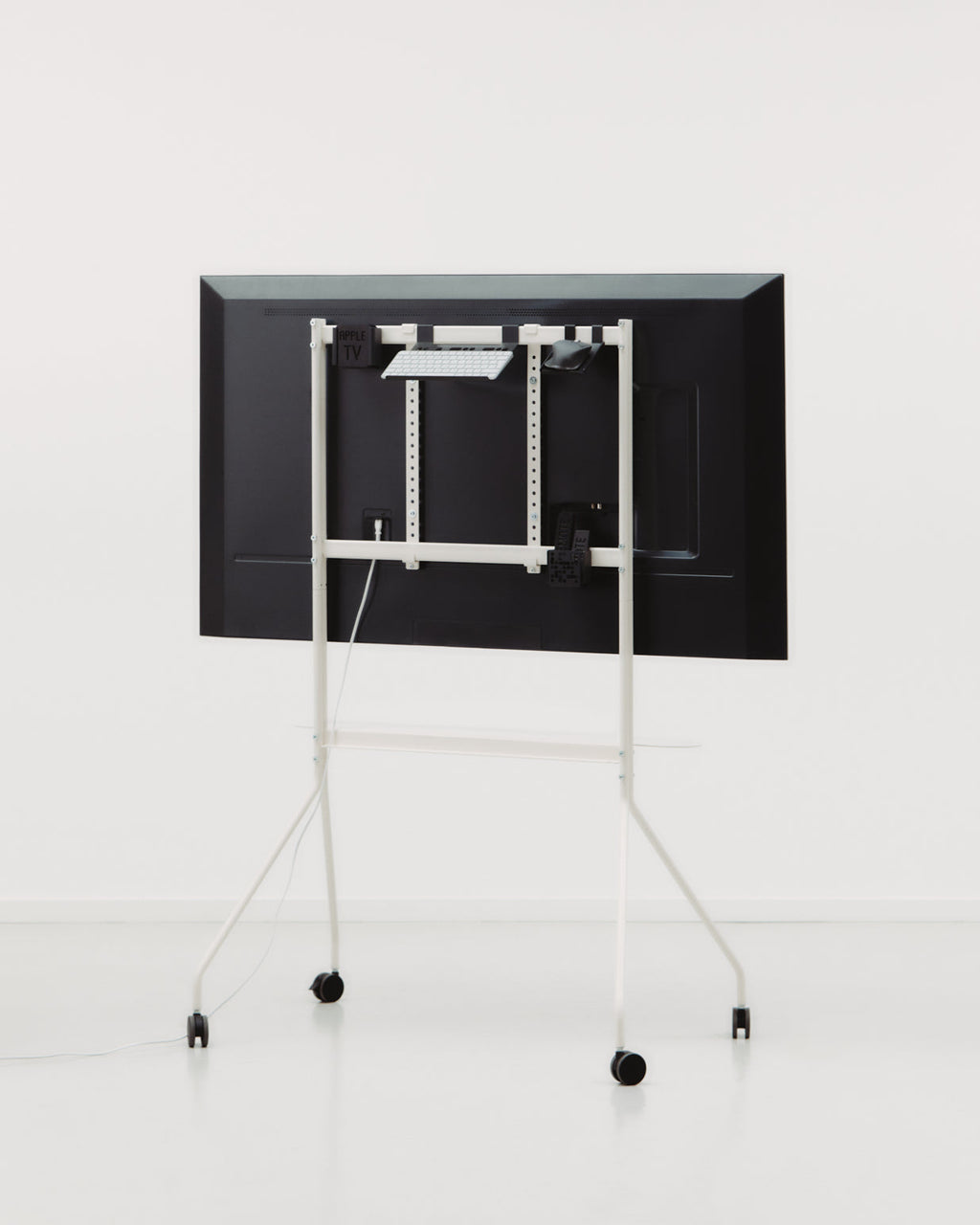 Rear view of Moon PRO stand in Pearl in a white studio, mounted TV with keyboard shelf, cable management and casters