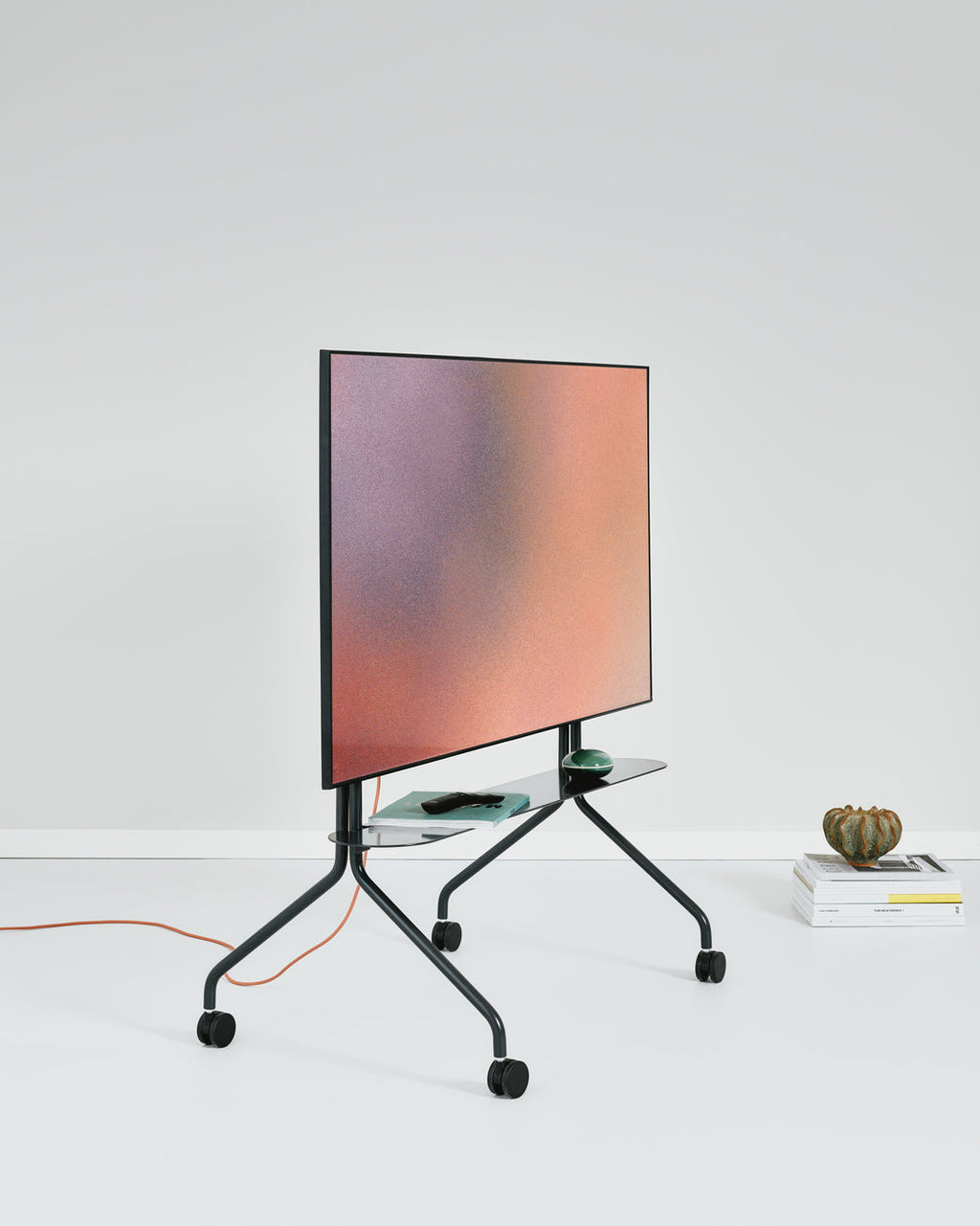 Moon in Charcoal rolling TV stand angled in a studio, mounted screen glowing, glass shelf and casters visible