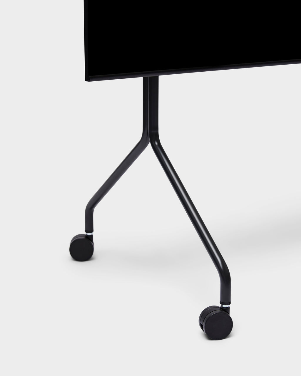 Close-up of Moon stand in Charcoal, showing angled tubular legs and black caster wheels supporting a mounted TV