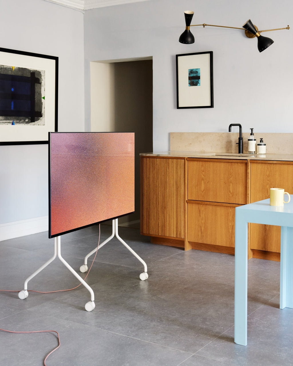 Moon in Pearl rolling TV stand with wheels holding a flatscreen in a modern kitchen with oak cabinets and blue table