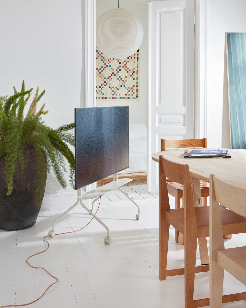 Moon in Pearl rolling TV stand holding a flatscreen in a bright white dining room beside a wood table and plant