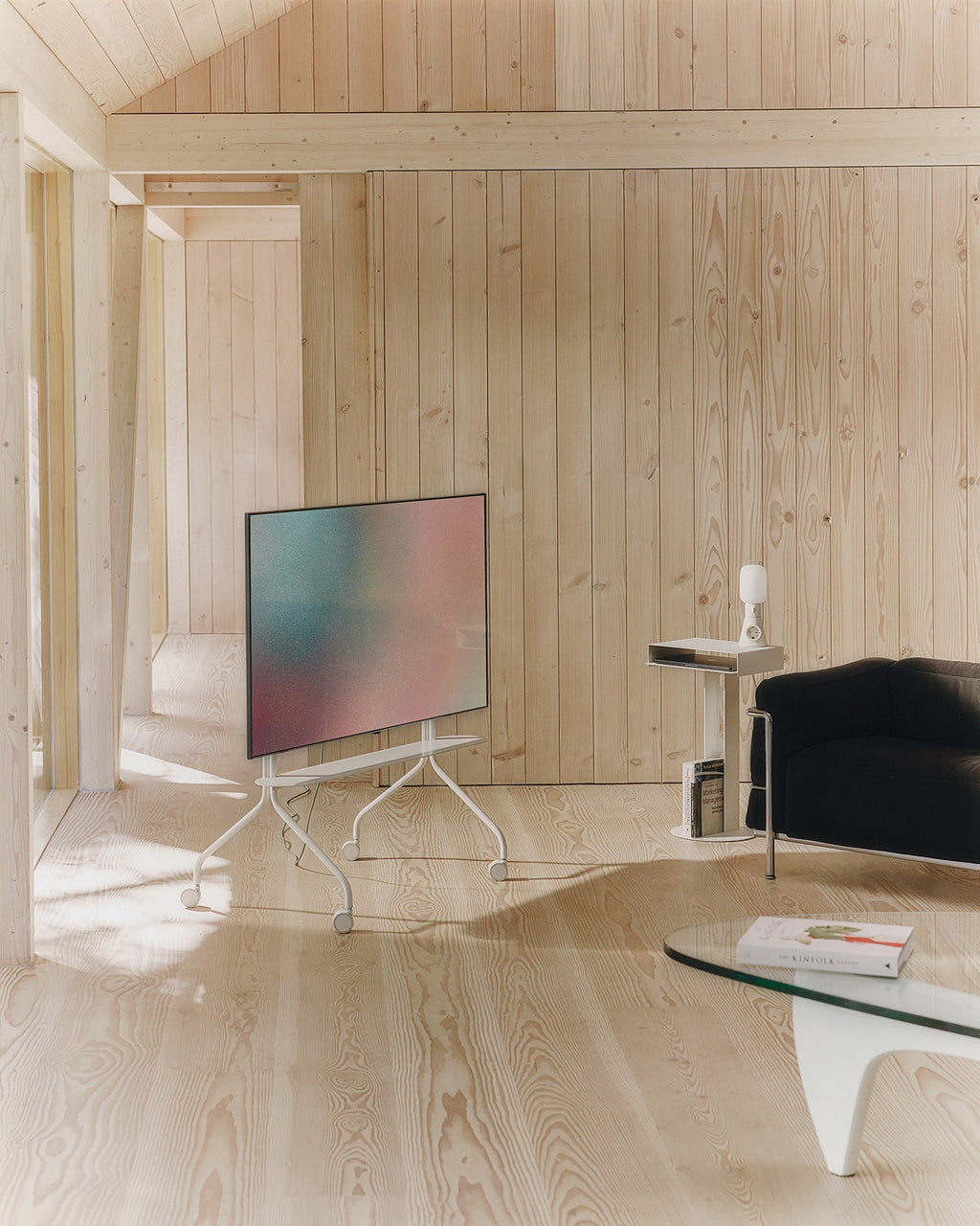 Moon in Pearl rolling TV stand holding a flatscreen in a sunlit pine-clad room, wheels visible, angled side view