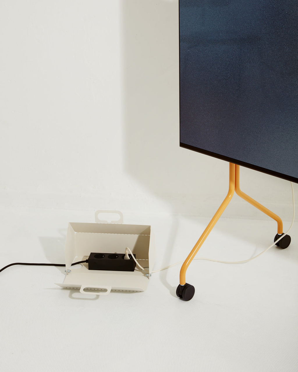 Moon stand in Apricot on wheels holding a TV, cable routed to a cream cable box with power strip on white floor