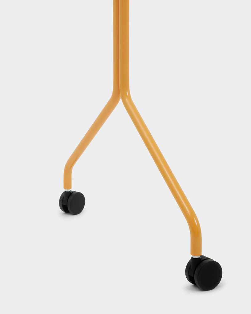 Close-up studio detail of the Moon stand in apricot, showing splayed tubular legs and black locking caster wheels
