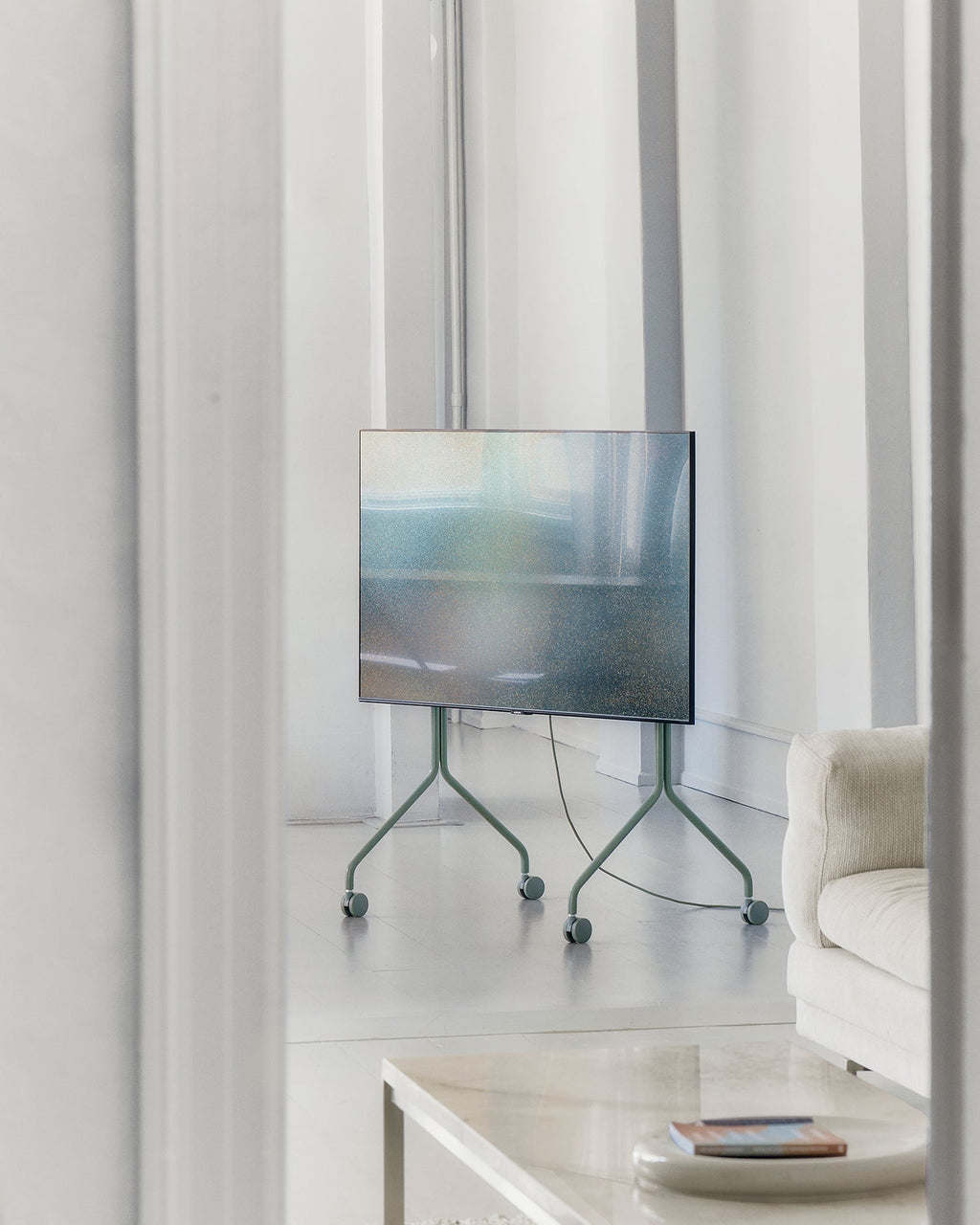 Moon TV stand in Mossy Green on wheels holding a flatscreen in a bright white living room beside a cream sofa