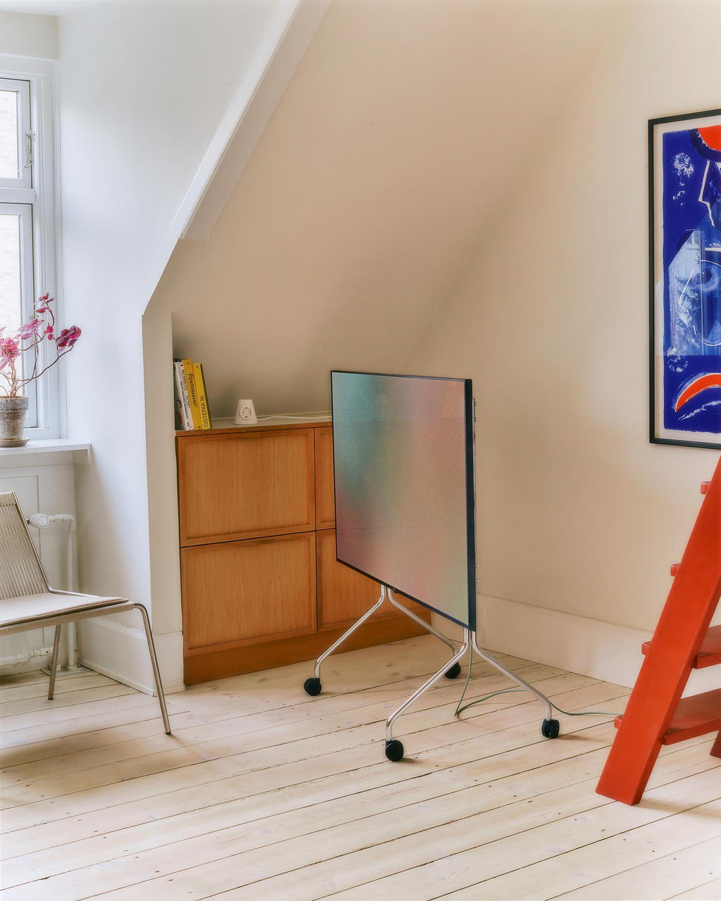 Moon in Chrome stand with wheels holding a folded-down TV in a bright attic room with wood floors