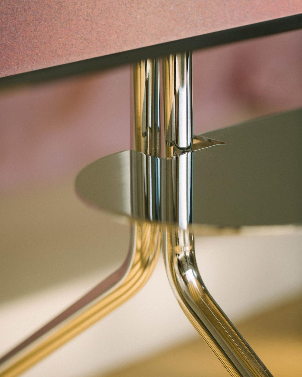 Close-up of the Moon in Chrome stand's polished column and splayed legs beneath a speckled pink tabletop