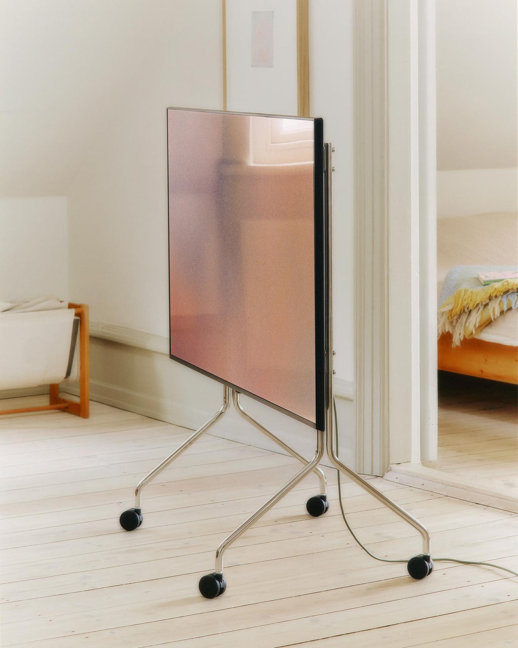 Moon in Chrome rolling TV stand with wheels holding a flatscreen in a bright wood-floored bedroom doorway