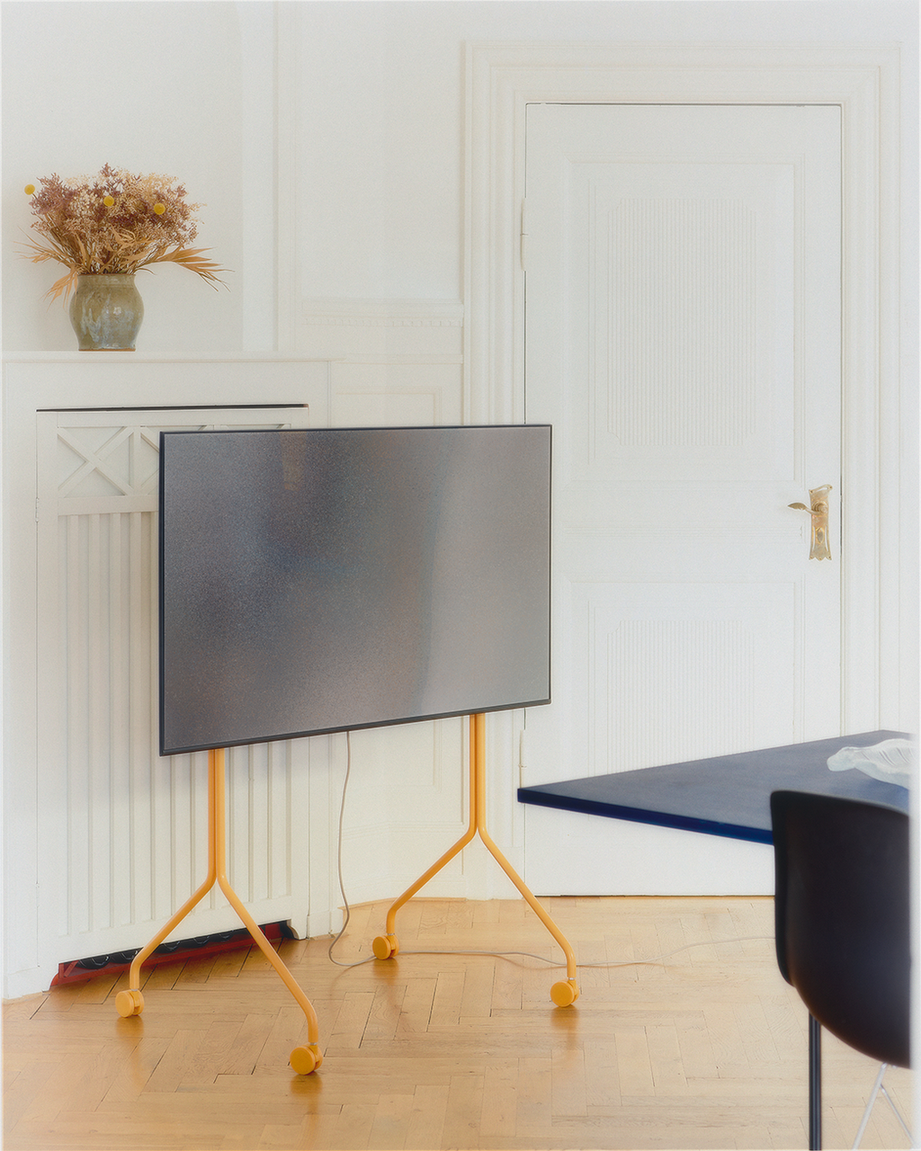 Moon Tall stand in Apricot on wheels holding a flat-screen TV in a bright room with parquet floor and blue table