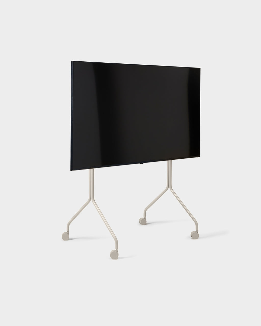 Moon Tall stand in Oat shown at an angle in studio, holding a large flat-screen TV on slim wheeled legs
