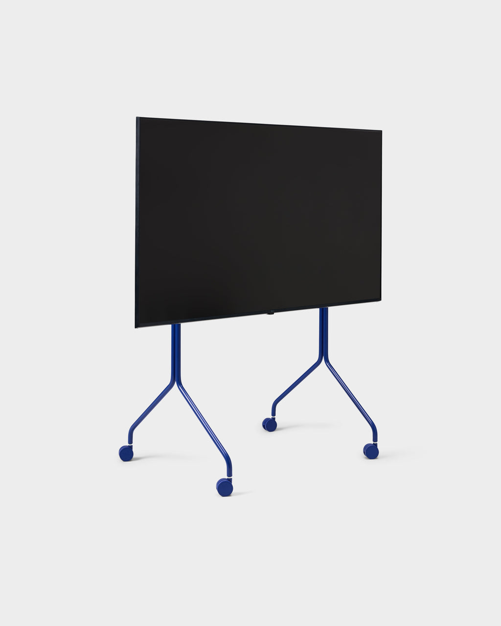 Moon Tall stand in Ultra Marine holding a flat-screen TV, angled studio view showing splayed legs and locking wheels