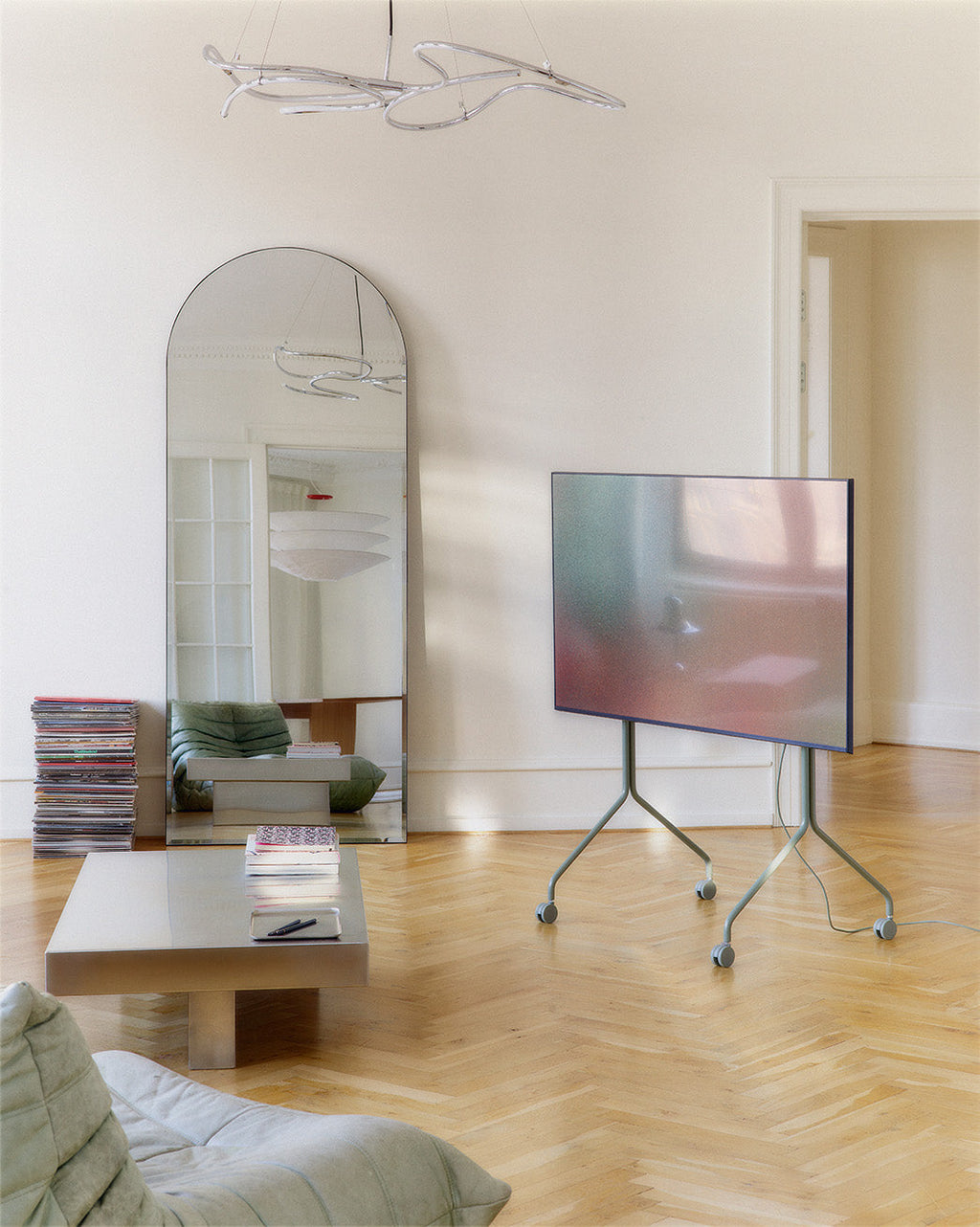 Moon Tall stand in Mossy Green on wheels holding a TV in a bright living room with arched mirror and parquet floor