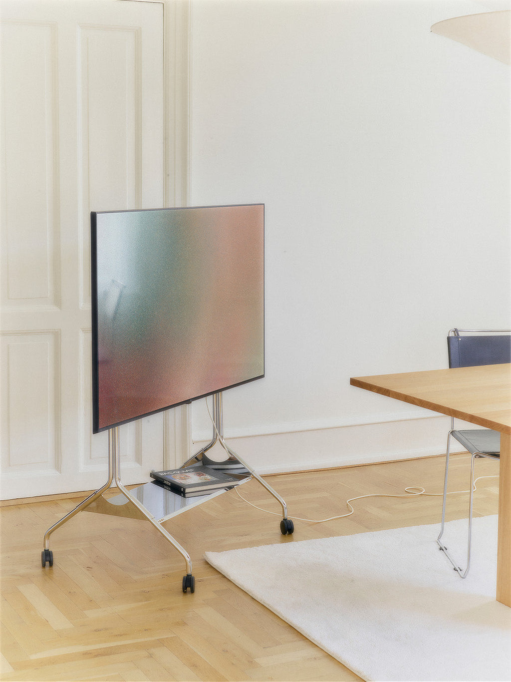 Moon Tall chrome TV stand on wheels holding a large screen in a bright paneled room with oak floor and dining table