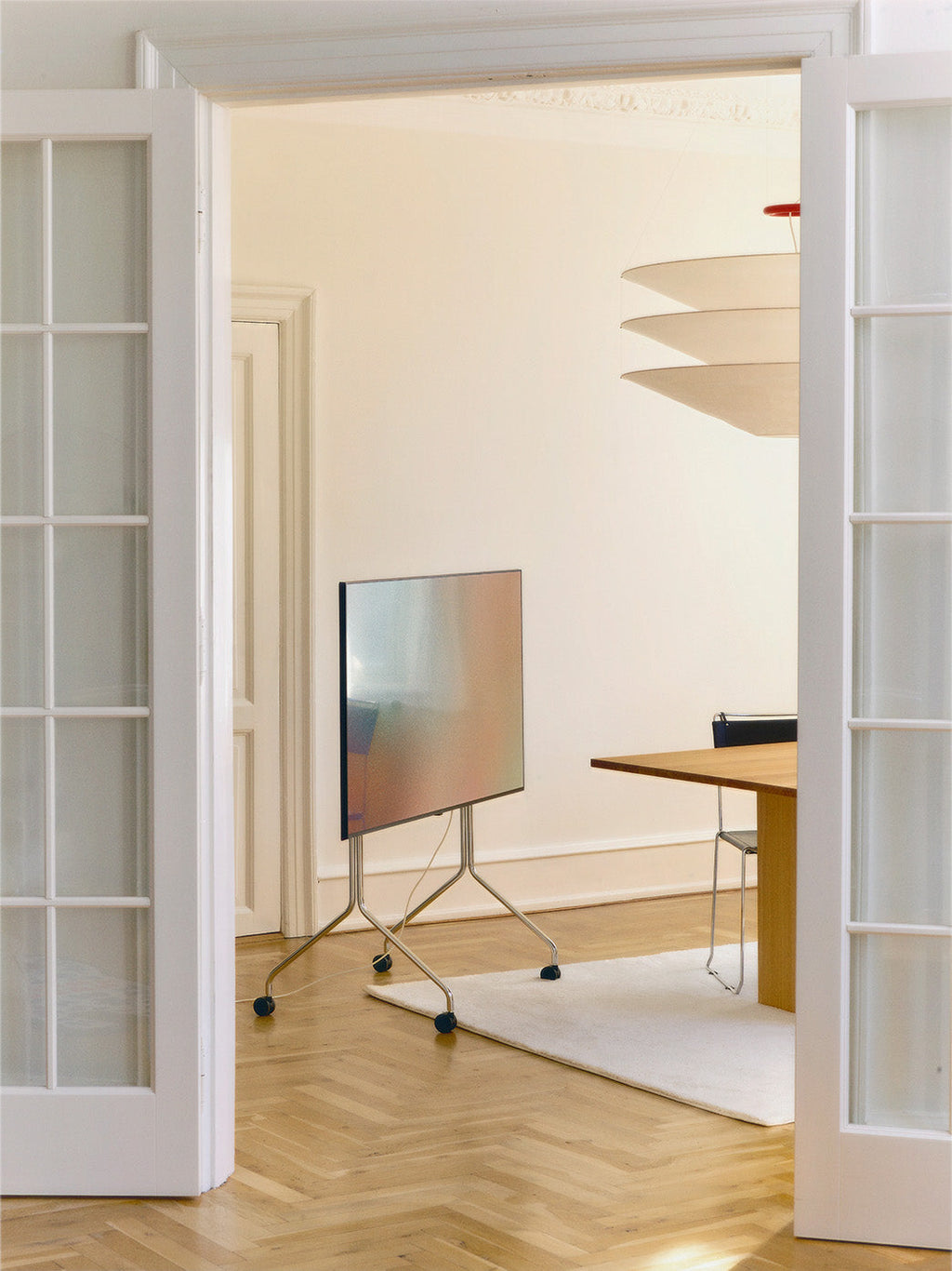 Moon Tall in Chrome rolling TV stand with wheels holding a flatscreen in a bright herringbone-floor living room