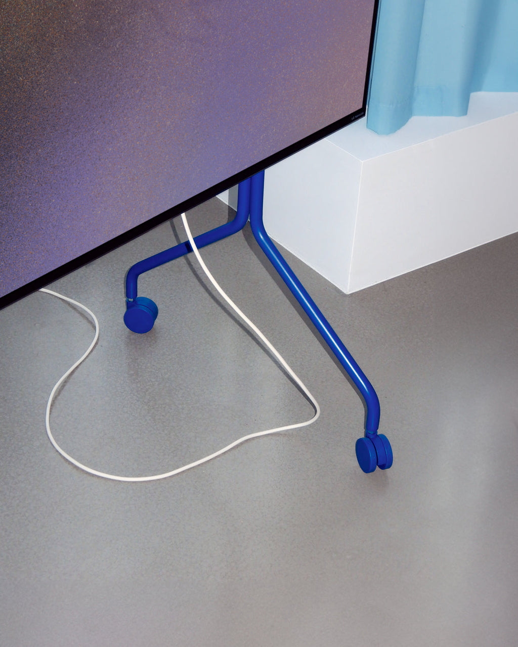 Ultra Marine Wheels on a blue TV stand's base, close-up floor-level view with white power cable trailing across grey floor