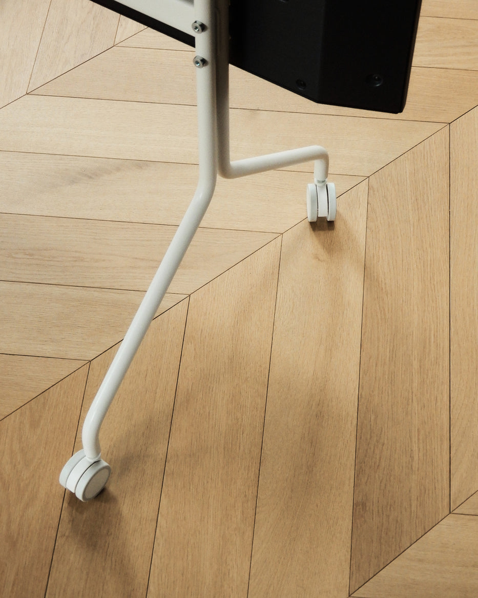 Close-up of Pearl Wheels casters on a white TV stand base, shown on herringbone wood flooring in a bright room