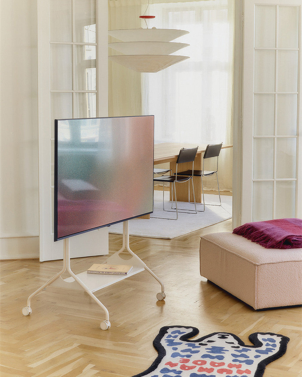 Moon Tray Shelf in Pearl holding books on a rolling TV stand in a sunlit living room with herringbone floors